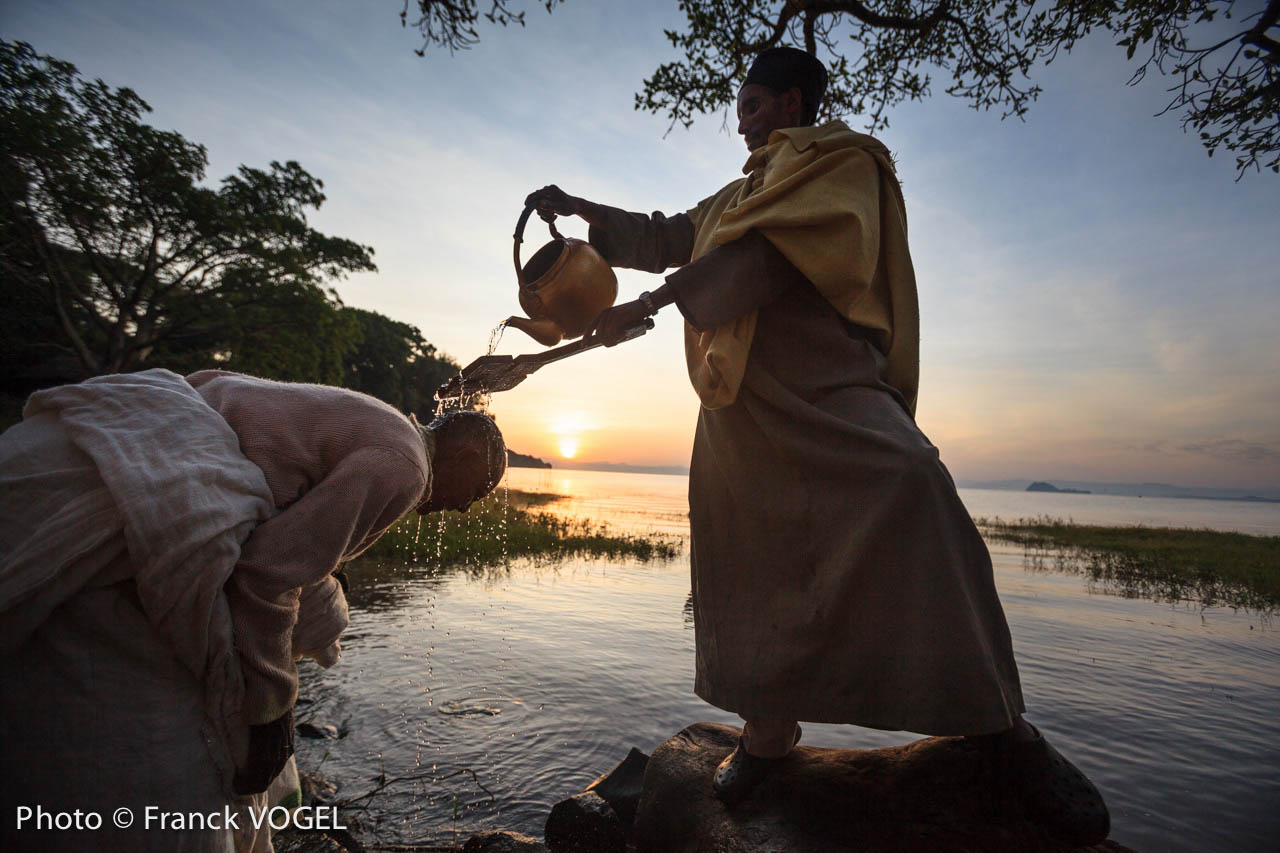 <p>Ethiopia – After the Divine Liturgy, lake Tana’s water is blessed by a priest from the nearby Orakidanu Bret monastery and sprinkled on the crowd. Some pilgrims immerse themselves, symbolically renewing their baptismal vows. Timkat is Ethiopian most important orthodox celebration. It symbolizes both Jesus baptism in the Jordan river and Epiphany. It takes place on January 19 (the 20th for leap years) all over the country. On Timkat’s eve, a colorful and joyful procession starts from Orakidanu Bret monastery on Zege peninsula, near Bahir Dar. A priest holds the Tabot, which represents the manifestation of Jesus as the Messiah when he came to the Jordan for baptism. When the crowd reaches lake Tana – source of the Blue Nile – they pray and sing all night long. At 4am, the lake’s water is blessed by priests and sprinkled on the crowd. Some pilgrims immerse themselves, symbolically renewing their baptismal vows.</p>
<p>Lors de la fête religieuse de Timqet (Pâques orthodoxe) sur la presqu’île de Zege au monastère Orakidanu Bret en Ethiopie. Après avoir veillé toute le nuit au bord du lac Tana à la belle étoile – il fait un froid de canard. Au petit matin, les croyants vont se faire asperger d’eau en rentrant dans l’eau du lac sacré…source du Nil Bleu et source de vie. Le Timqet est la célébration éthiopienne orthodoxe à la fois du baptême de Jésus dans le Jourdain et de l’Épiphanie. Elle a lieu le 19 janvier (le 20 pour les années bissextiles). La fête est connue pour sa reconstitution rituelle du baptême (similaire aux reconstitutions de nombreux pèlerins chrétiens en Terre Sainte lorsqu’ils se rendent au Jourdain). Timqet est une des cérémonies durant laquelle les tabots (répliques de l’Arche de l’Alliance) sont retirés des églises pour être vus par la foule, des tissus sont toutefois enroulés autour. Pendant la procession, qui a lieu la veille, les prêtres, vêtus de costumes colorés, portent les tabots sur leur tête pour les amene</p>
image Nile-Franck-Vogel-8